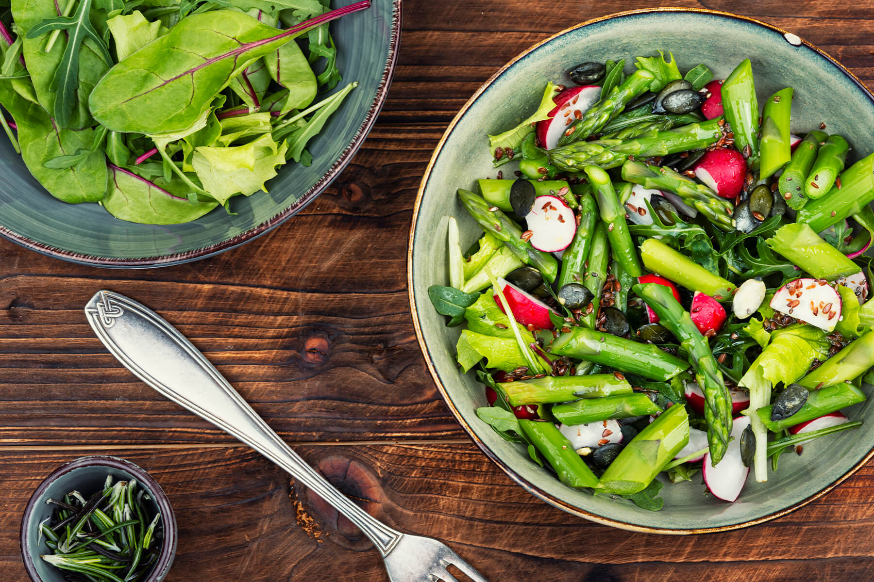 Grüner Spargelsalat mit Radieschen, Rucola und Kürbiskernen in einer Schüssel, daneben eine Schale Blattsalat