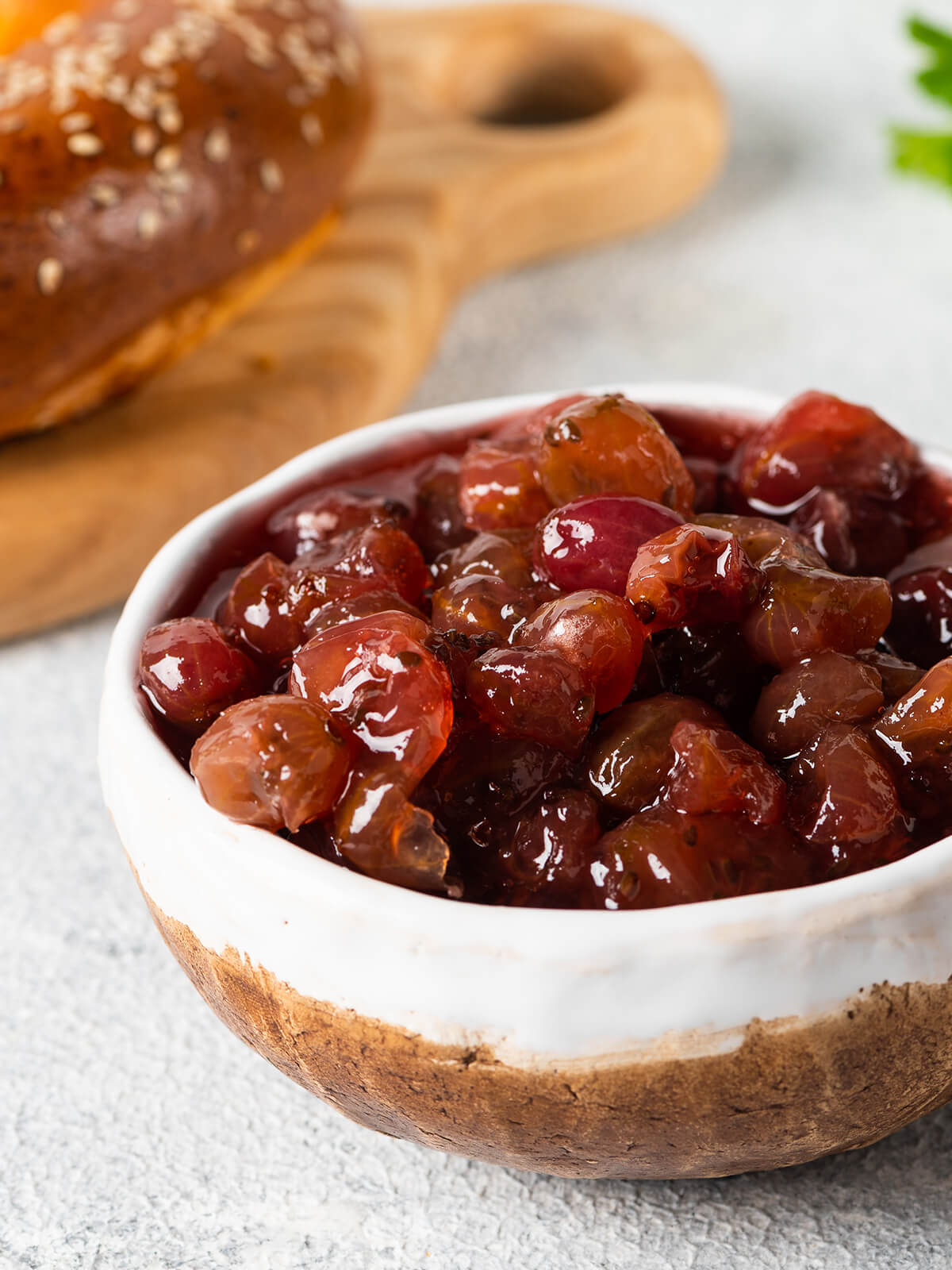 Stachelbeer-Konfitüre mit ganzen Beeren in einer Schale, dahinter ein Sesambrötchen
