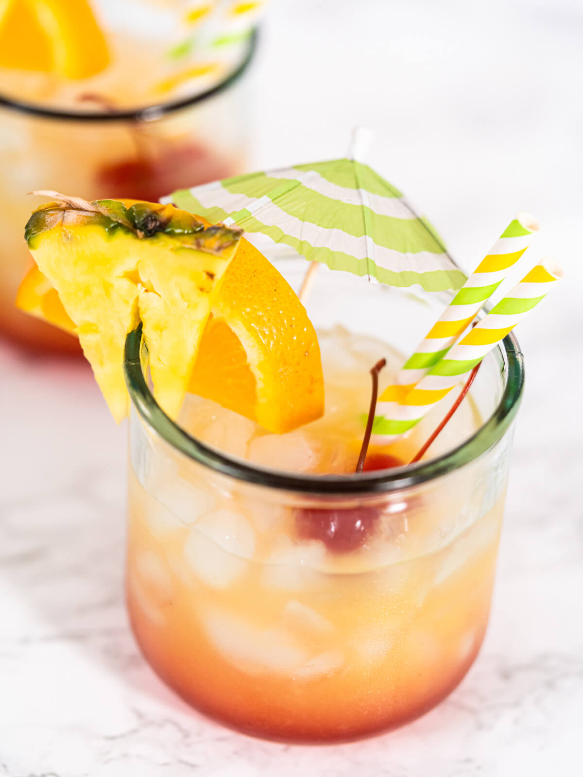 Sunset-Cocktail mit deutlichem Farbverlauf von Rot unten zu Gelb oben, garniert mit Orange, Ananas und Cocktailschirmchen