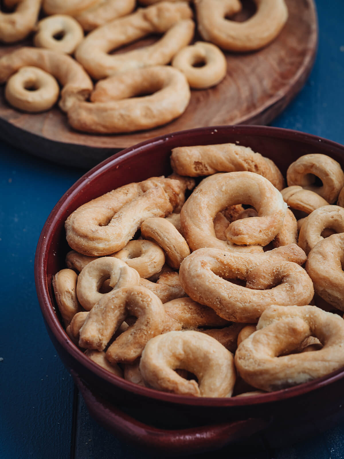 Herzhafte goldbraune Taralli Pugliesi in einer Terrakotta-Schale und auf einem Holzteller auf blauem Tisch