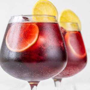 Zwei Stielgläser mit rubinrotem Tinto de Verano auf Eis, garniert mit Zitronen- und Orangenscheiben, feine Bläschen und beschlagene Gläser