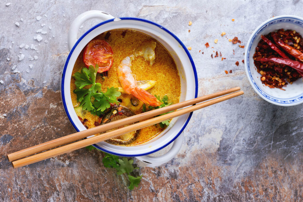Cremige Tom-Yam-Suppe mit Garnele, gerösteter Tomate, Shiitake und Kräutern von oben, daneben getrocknete Chili