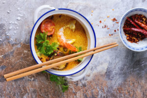 Cremige Tom-Yam-Suppe mit Garnele, gerösteter Tomate, Shiitake und Kräutern von oben, daneben getrocknete Chili
