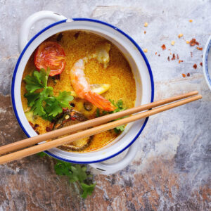 Cremige Tom-Yam-Suppe mit Garnele, gerösteter Tomate, Shiitake und Kräutern von oben, daneben getrocknete Chili
