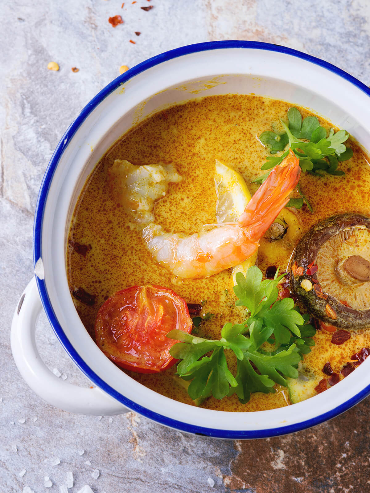 Nahaufnahme der Tom-Yam-Suppe mit Garnele, gerösteter Tomate, Shiitake und frischen Kräutern in cremig-oranger Brühe