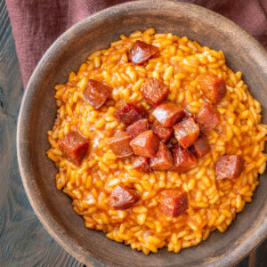 Cremiges Tomaten-Chorizo-Risotto mit knusprig gebratenen Chorizo-Würfeln in einer dunklen Keramikschale