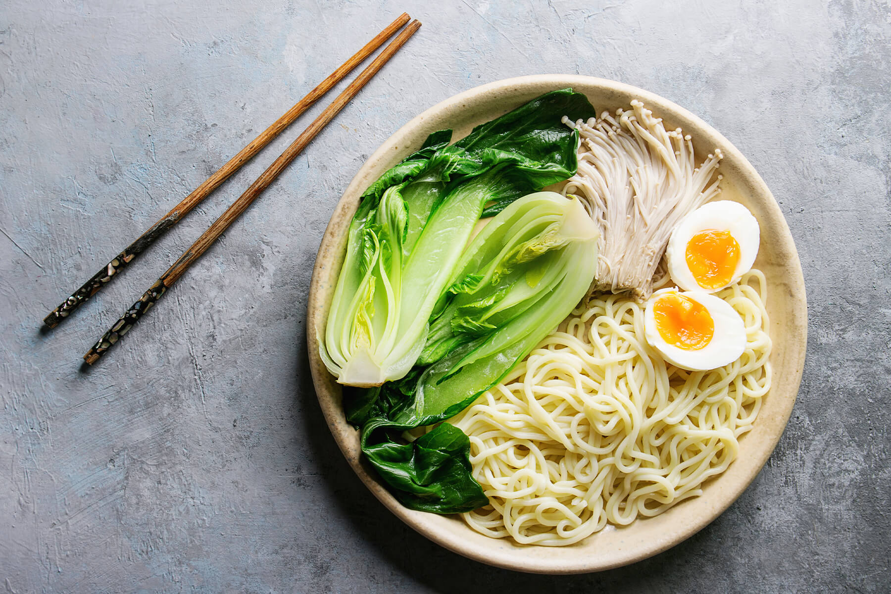 Angerichteter Teller mit dicken Udon-Nudeln, halbiertem Pak Choi, Enoki-Pilzen und weichem Ei