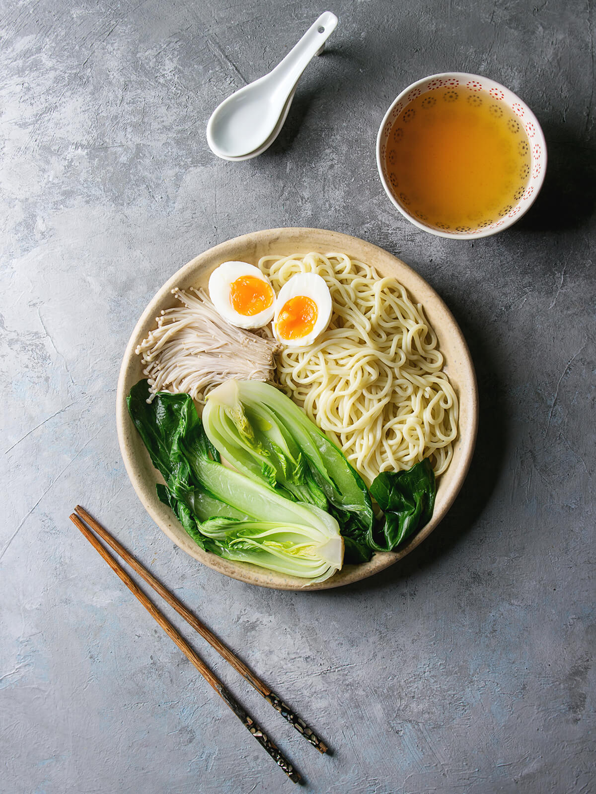 Teller mit Udon, Pak Choi, Enoki und weichem Ei, daneben ein Schälchen mit klarer Brühe