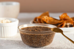 Glasschale mit veganem Chia-Kaviar vorne, links ein weißes Förmchen mit veganer Frischkäse-Creme, im Hintergrund unscharf ein Teller mit goldbraunen Crêpes, ein goldener Löffel rechts an der Schale