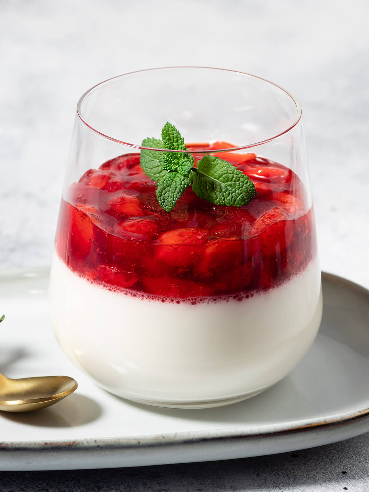 Vegane Kokos-Panna-Cotta mit Erdbeer-Belag im Glas, garniert mit einem Zweig Minze