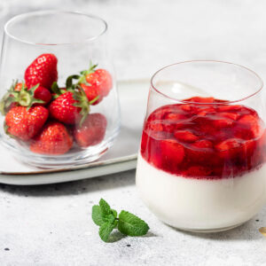 Vegane Kokos-Panna-Cotta mit Erdbeeren im Glas, daneben ein Glas mit frischen Erdbeeren und Minze