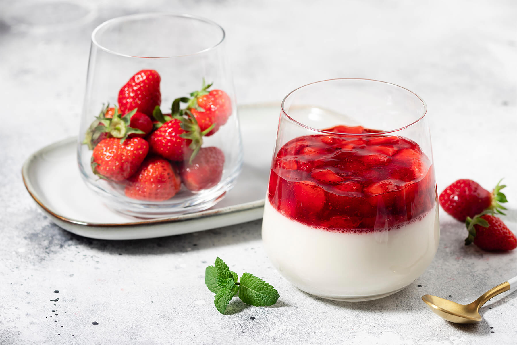 Vegane Kokos-Panna-Cotta mit rotem Erdbeer-Belag im Glas, daneben ein Glas voller frischer Erdbeeren