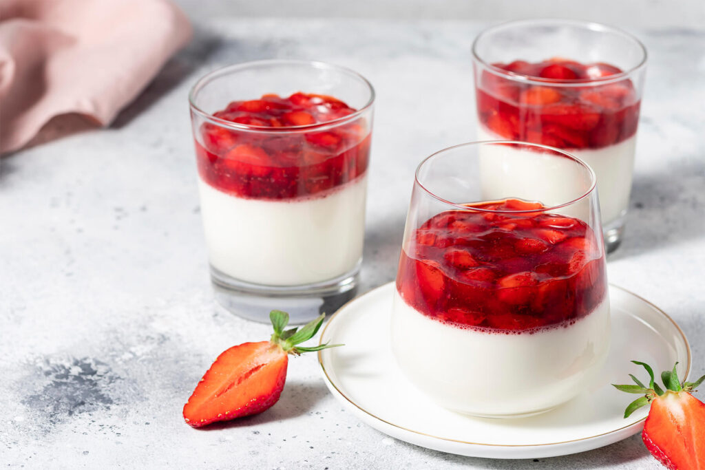 Drei Gläser vegane Kokos-Panna-Cotta mit Erdbeer-Belag, angerichtet mit frischen Erdbeeren
