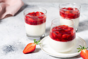 Drei Gläser vegane Kokos-Panna-Cotta mit Erdbeer-Belag, angerichtet mit frischen Erdbeeren