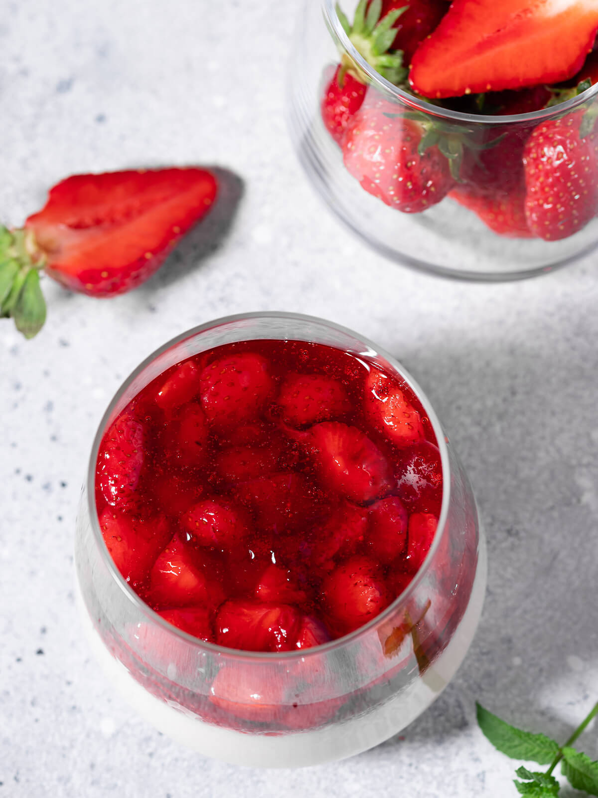 Blick von oben auf ein Glas vegane Kokos-Panna-Cotta mit glänzendem Erdbeer-Belag, daneben frische Erdbeeren