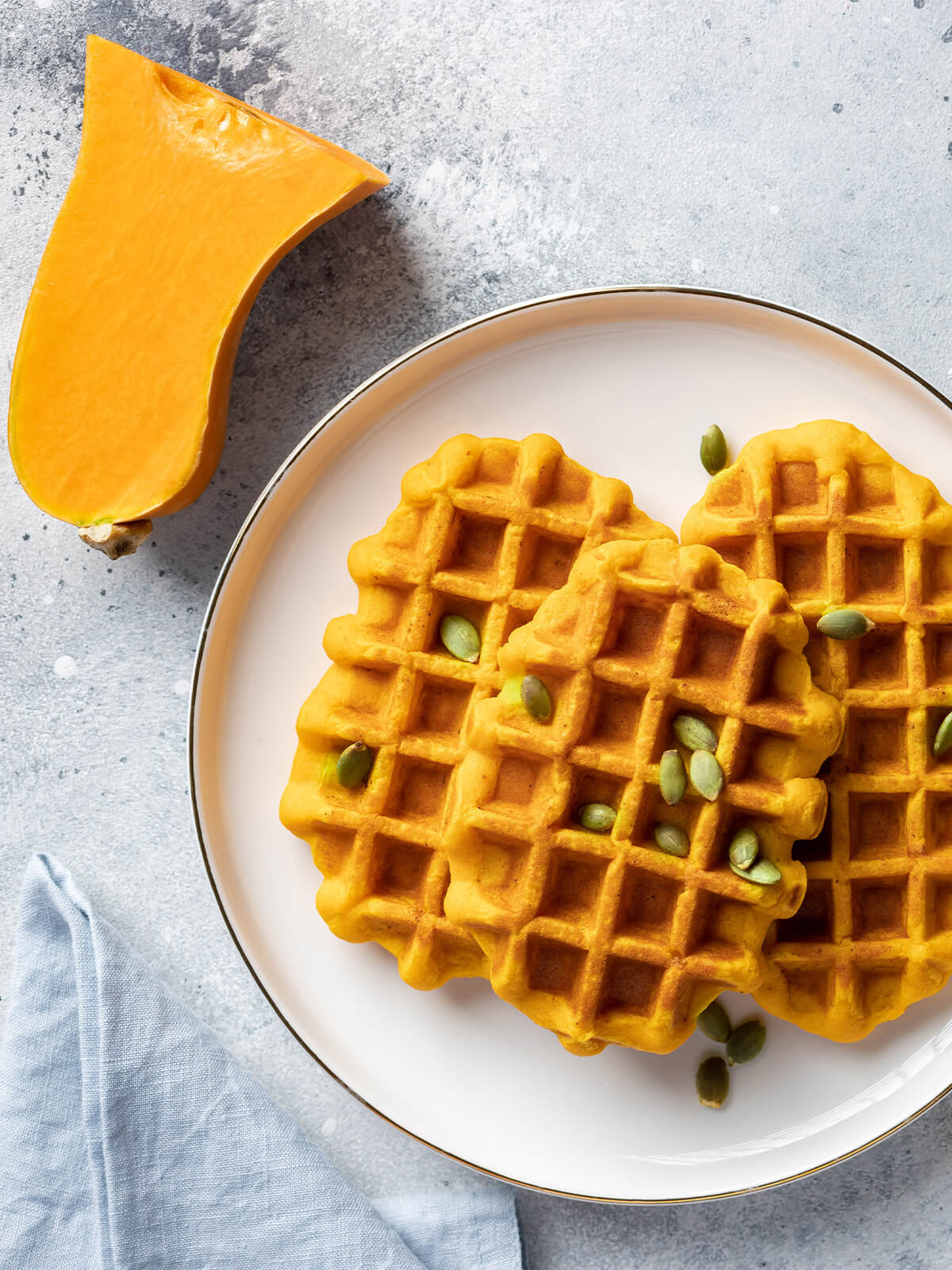 Vegane Kürbiswaffeln auf einem weißen Teller mit halbem Butternut-Kürbis und Kürbiskernen