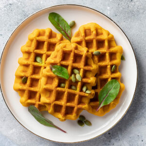 Vegane Kürbiswaffeln auf einem weißen Teller, garniert mit Kürbiskernen und frischen grünen Blättern