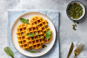 Vegane Kürbiswaffeln auf einem Teller, angerichtet mit gerösteten Kürbiskernen und frischen grünen Blättern