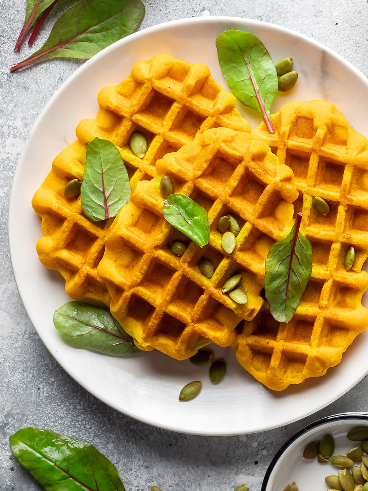 Nahaufnahme veganer Kürbiswaffeln mit gerösteten Kürbiskernen und frischen grünen Blättern