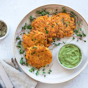 Vegane Süßkartoffel-Puffer auf einem Teller mit cremigem Avocado-Dip und frischer Kresse