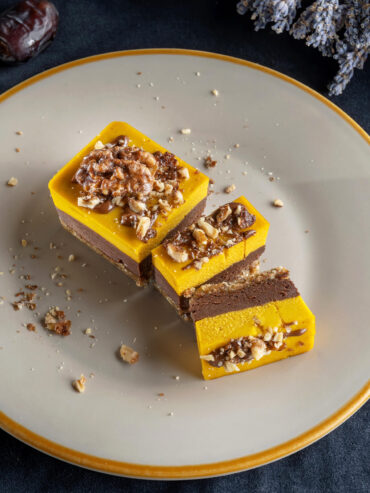 Vegane Kürbis-Schoko-Riegel mit Dattel-Nuss-Boden, Schokoladencreme und leuchtender Kürbisschicht, garniert mit Walnüssen