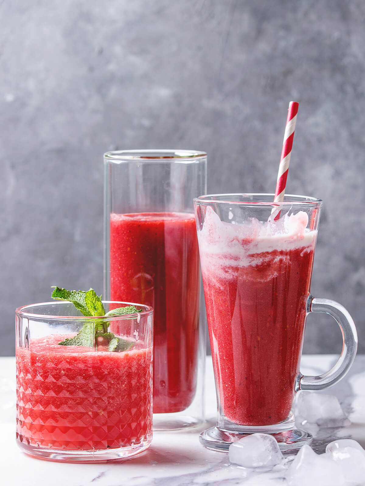 Drei Gläser roter Frucht-Smoothie mit Wassermelone und Beeren, garniert mit Minze und Strohhalm