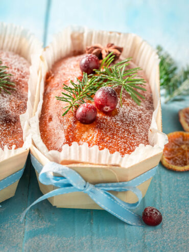 Weihnachtlicher Früchtekuchen in kleiner Holzform, verziert mit Puderzucker, Cranberries, Sternanis und Tannenzweig