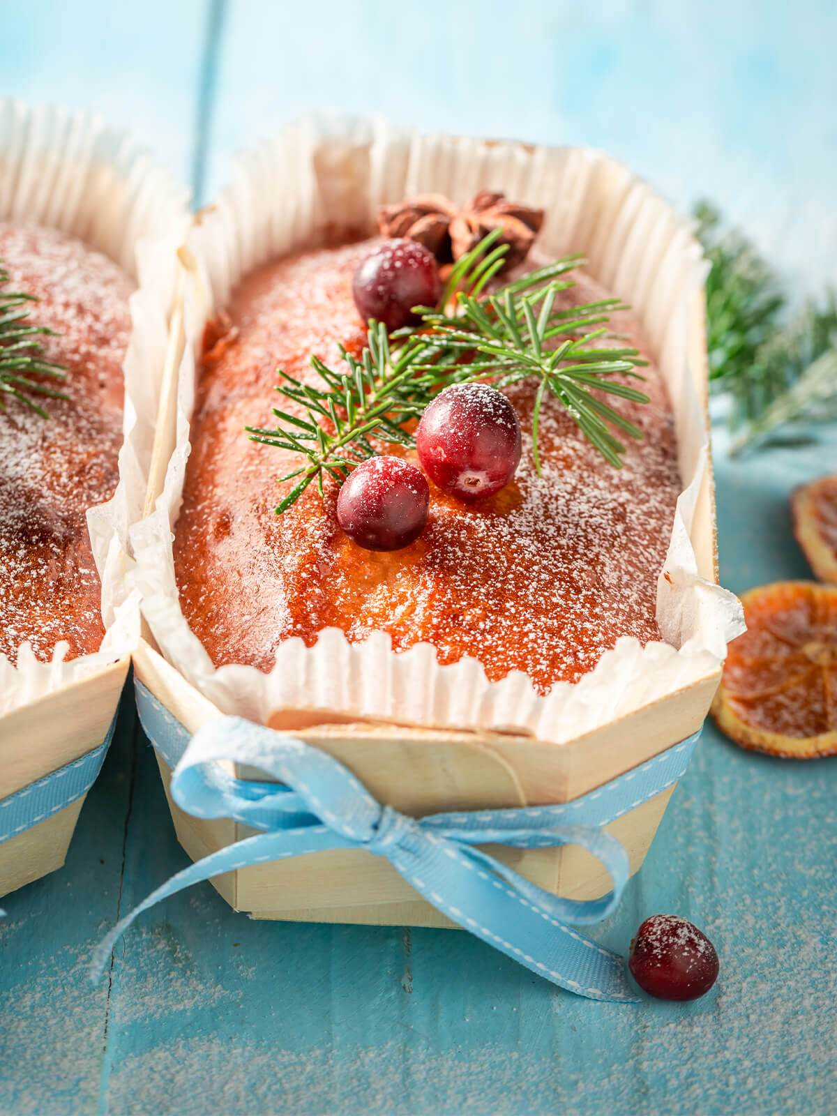 Weihnachtlicher Früchtekuchen in kleiner Holzform, verziert mit Puderzucker, Cranberries, Sternanis und Tannenzweig