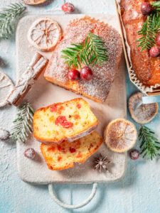 Angeschnittener weihnachtlicher Früchtekuchen mit kandierten Kirschen und Orangeat im Teig, bestäubt mit Puderzucker