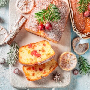 Angeschnittener weihnachtlicher Früchtekuchen mit kandierten Kirschen und Orangeat im Teig, bestäubt mit Puderzucker