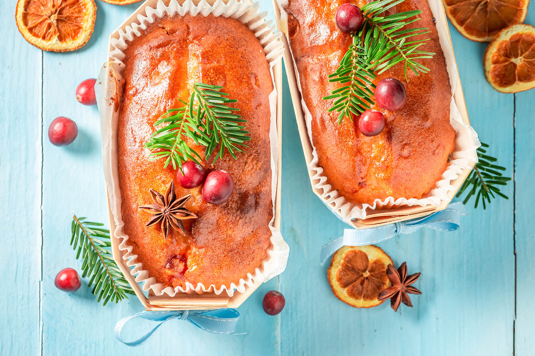 Zwei kleine weihnachtliche Früchtekuchen in Holzformen von oben, glänzend glasiert und verziert mit Tannenzweigen, Cranberries und Sternanis