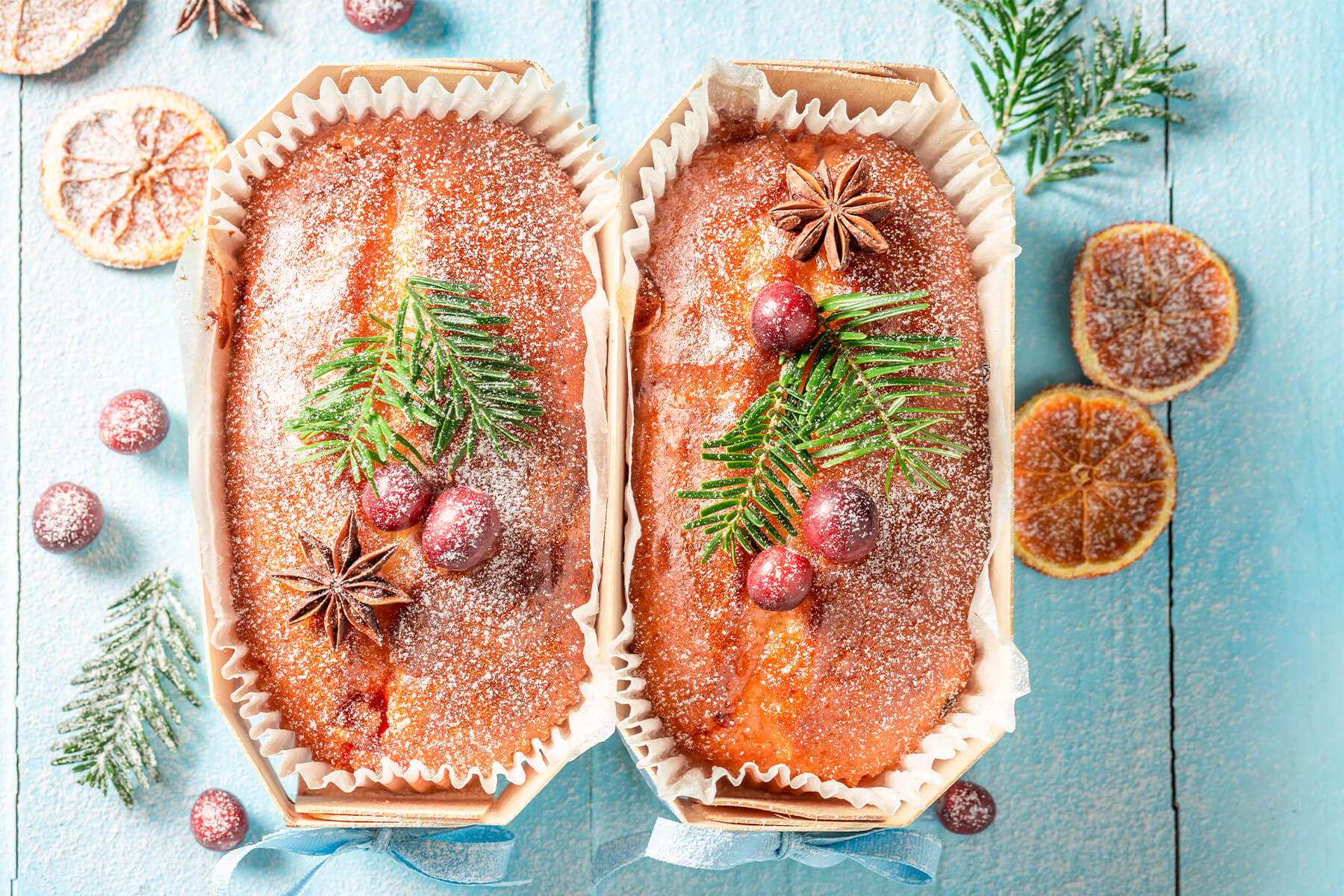 Zwei weihnachtliche Früchtekuchen in Holzformen mit glänzender Oberfläche, Puderzucker und weihnachtlicher Dekoration von oben