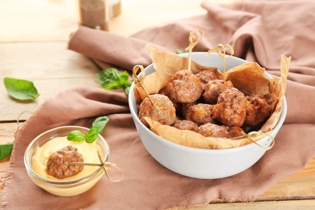 Gebackene Wurst-Käse-Bällchen in einer Schale, daneben ein Schälchen Dip