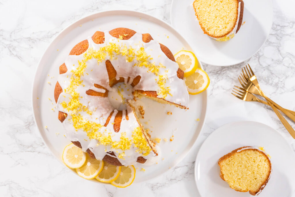 Angeschnittener Zitronen-Gugelhupf mit Glasur, zwei Stücke auf Tellern mit goldenen Gabeln