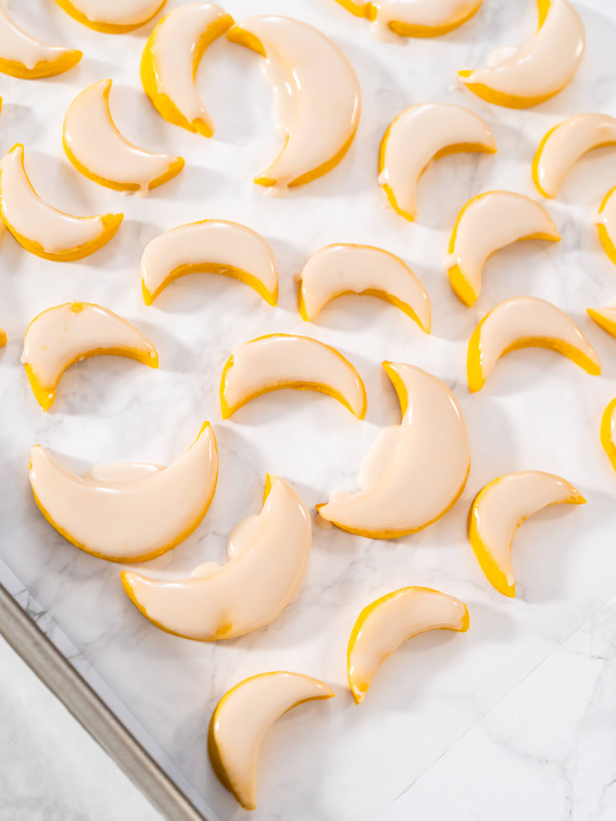 Viele glasierte Zitronen-Mond-Plätzchen mit glänzender Oberfläche auf heller Marmorfläche verteilt