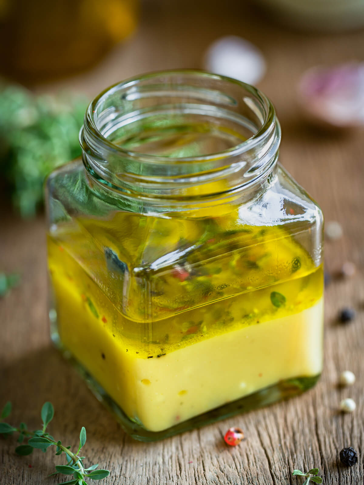 Klassische Zitronen-Thymian-Vinaigrette in einem eckigen Glas, in Öl- und Zitronenschicht getrennt, mit Thymian und bunten Pfefferkörnern