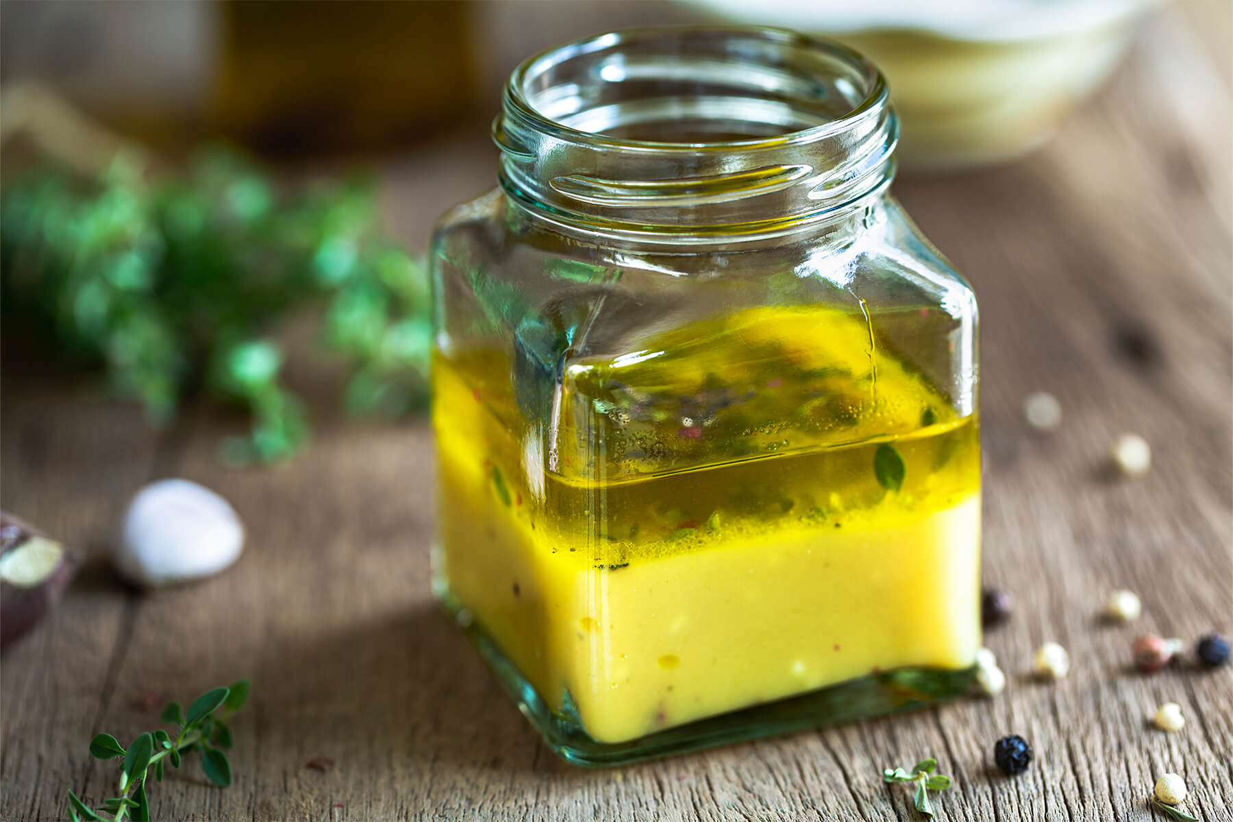 Zitronen-Thymian-Vinaigrette im eckigen Glas mit deutlich sichtbarer Trennung in eine untere Zitronenschicht und oberes Olivenöl mit Thymian