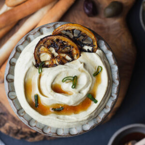 Cremiger Feta-Dip in einer Steingutschale mit karamellisierten Zitronenscheiben, Honig und Frühlingszwiebelgrün
