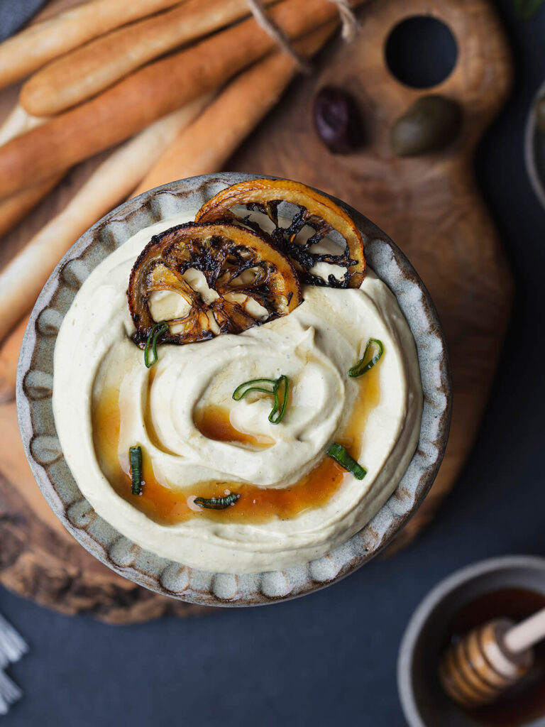 Cremiger Feta-Dip in einer Steingutschale mit karamellisierten Zitronenscheiben, Honig und Frühlingszwiebelgrün