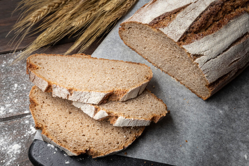 Fertig gebackenes Bauernbrot mit Sauerteig auf Backpapier, daneben zwei aufgeschnittene Scheiben