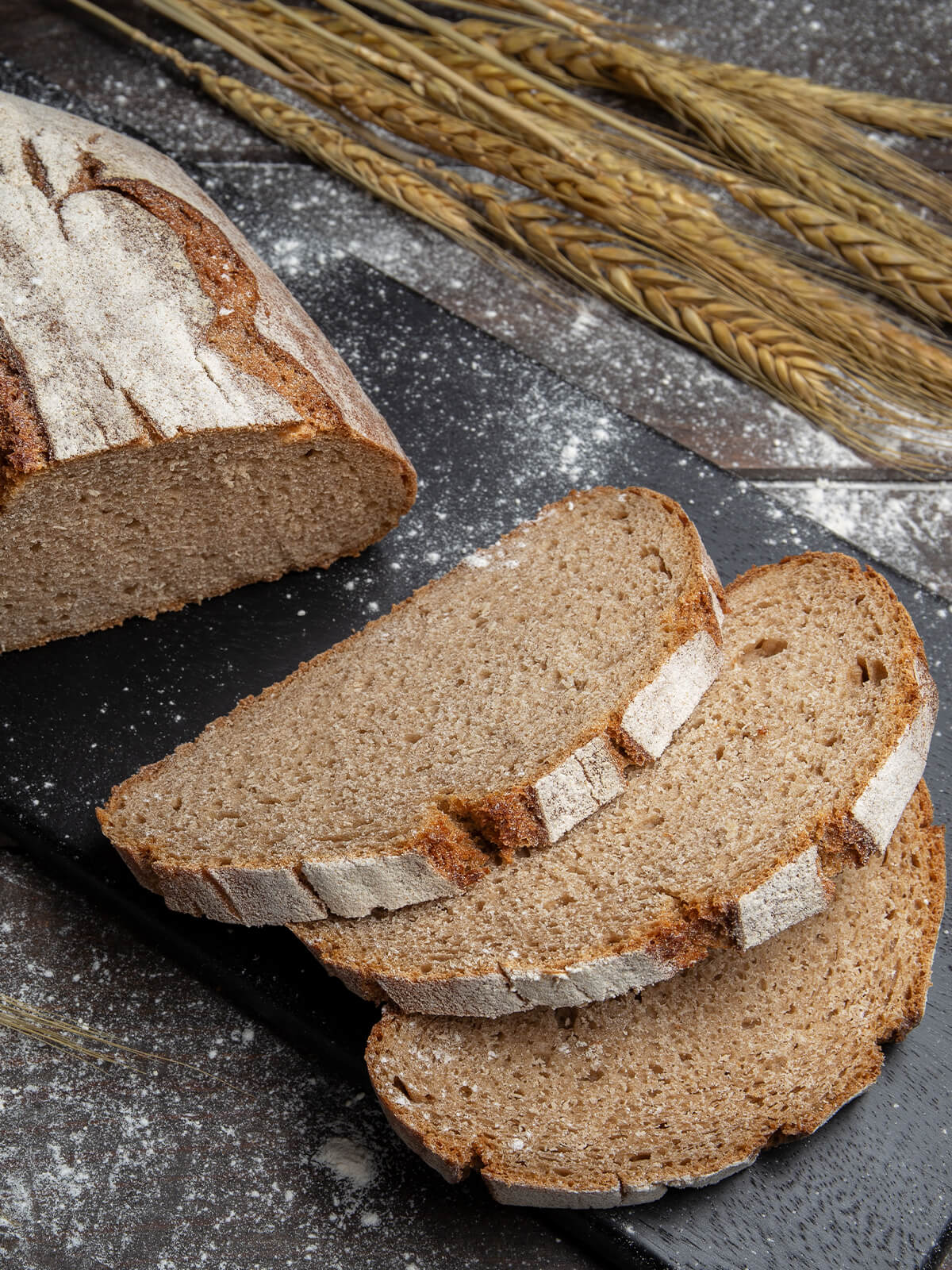 Angeschnittenes Bauernbrot mit Sauerteig und zwei Scheiben auf dunklem Schieferbrett