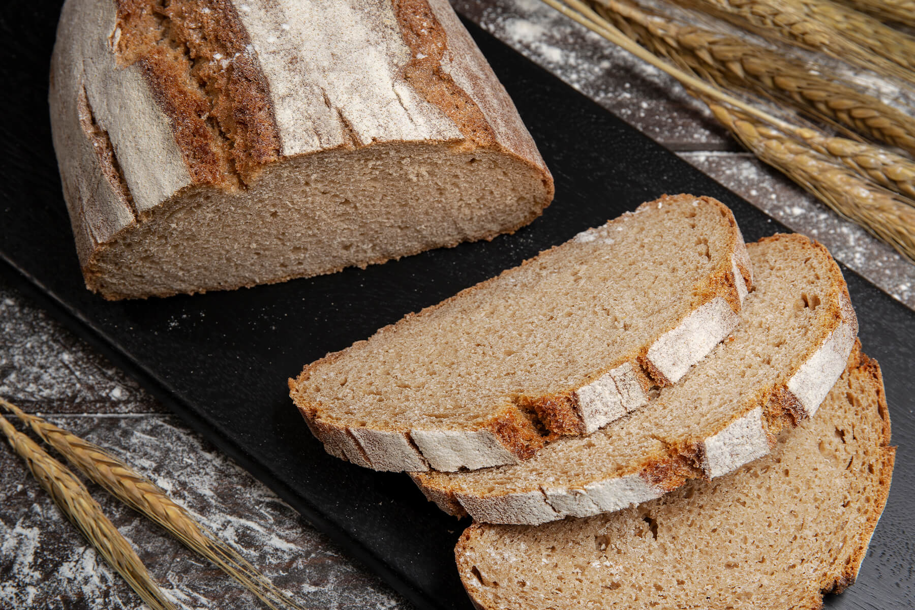 Angeschnittener Laib Bauernbrot mit Sauerteig neben zwei Scheiben mit feinporiger Krume