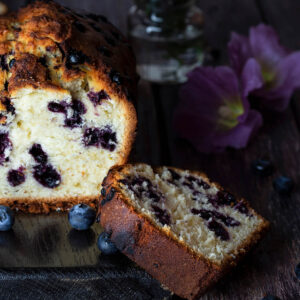 Angeschnittener Blaubeer-Limetten-Kastenkuchen mit ganzen Blaubeeren im hellen Butterteig