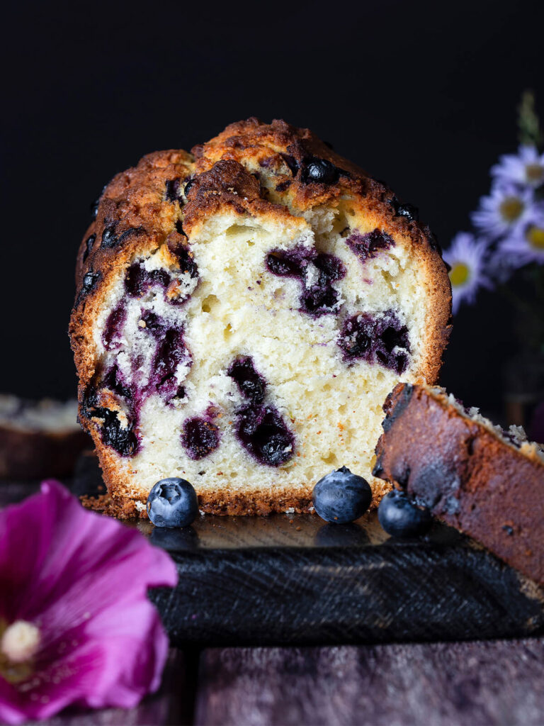 Aufrecht stehender angeschnittener Blaubeer-Limetten-Kastenkuchen mit ganzen Blaubeeren