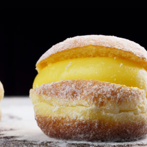 Aufgeschnittener brasilianischer Cremekrapfen mit dicker gelber Vanillecreme und Puderzucker