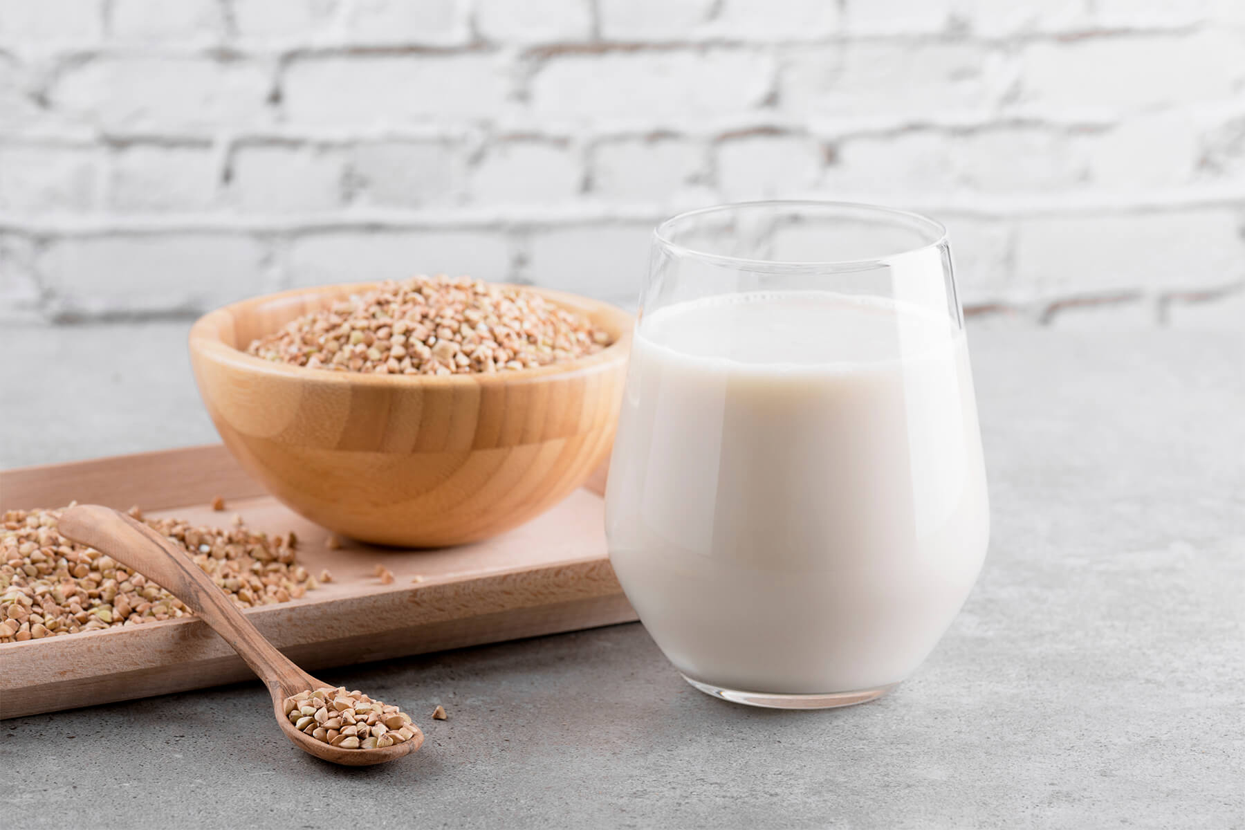 Schale mit blass beige-grünlichen Buchweizenkörnern neben einem Glas heller Pflanzenmilch