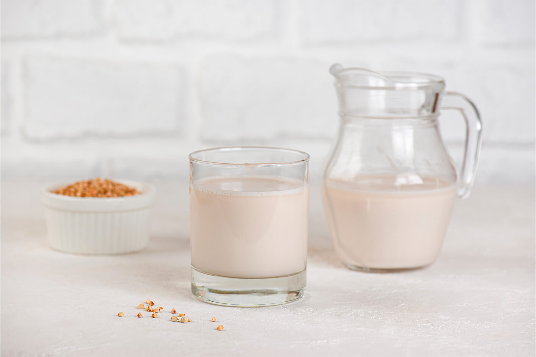 Kleine Schale mit rötlich-braunen gerösteten Buchweizenkörnern neben Glas und Krug mit Pflanzenmilch