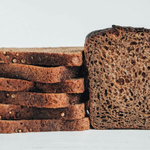 Gestapelte Scheiben dunkles Roggenbrot mit Koriandersamen auf der Kruste neben einem angeschnittenen Laib