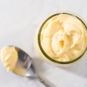 Cremige hellgelbe Frischkäse-Füllung in einem Glas, daneben ein Löffel