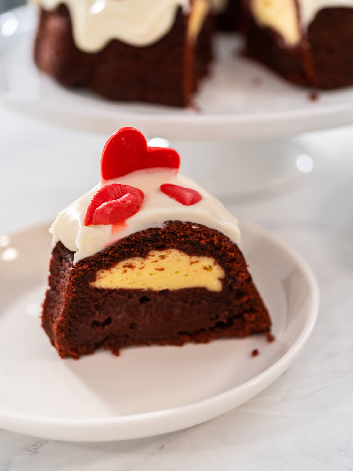 Kuchenstück mit hellgelbem Frischkäse-Kern im dunklen Teig auf einem weißen Teller